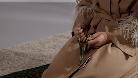 Nahaufnahme-Einer-Muslimischen-Frau-Mit-Gebetskette-Zu-Hause,-Die-Kniend-Auf-Einer-Gebetsmatte-Betet